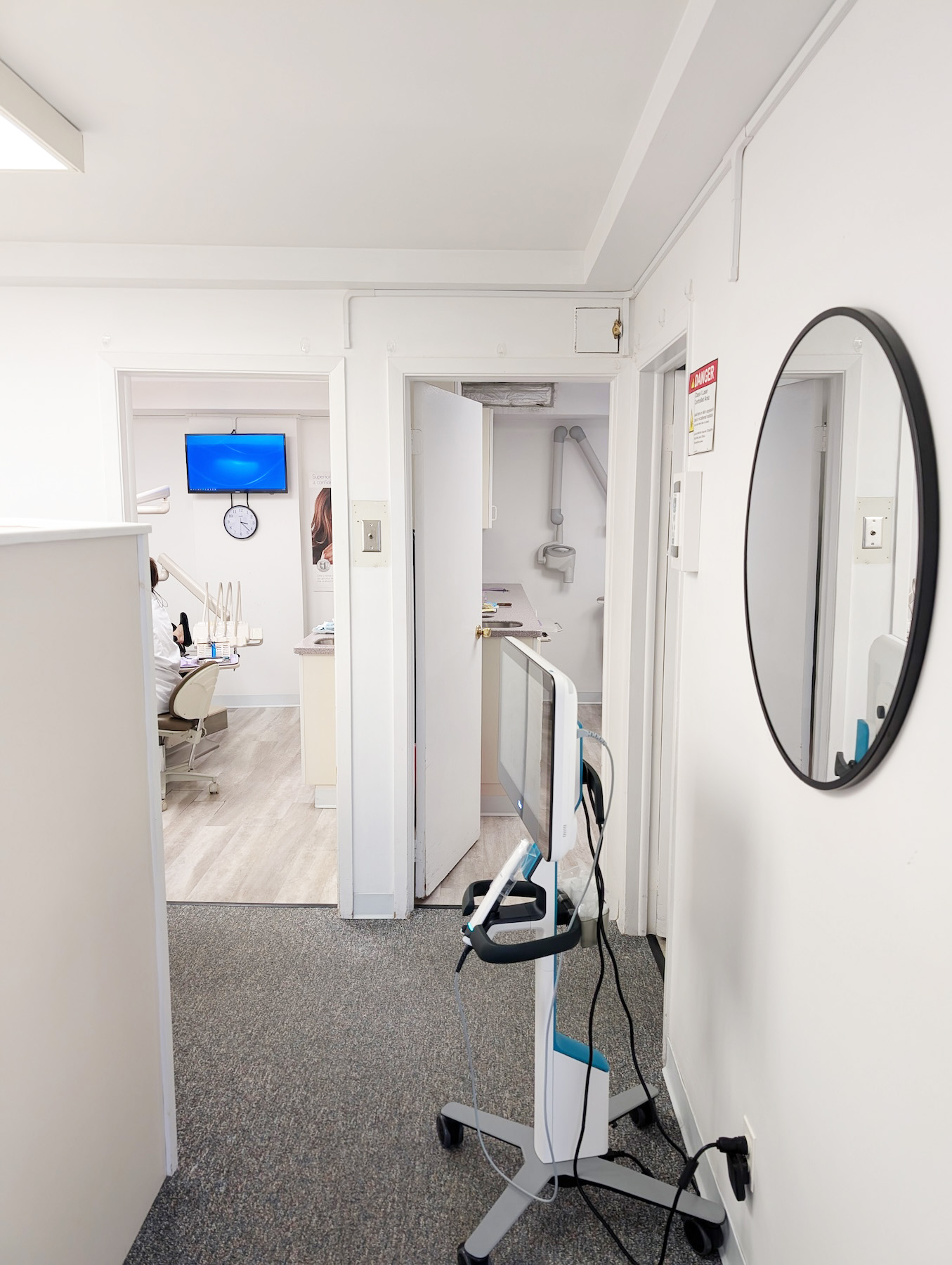 The image shows an interior space with a door leading into a room equipped for dental procedures, featuring a large mirror on the wall and various dental equipment visible.