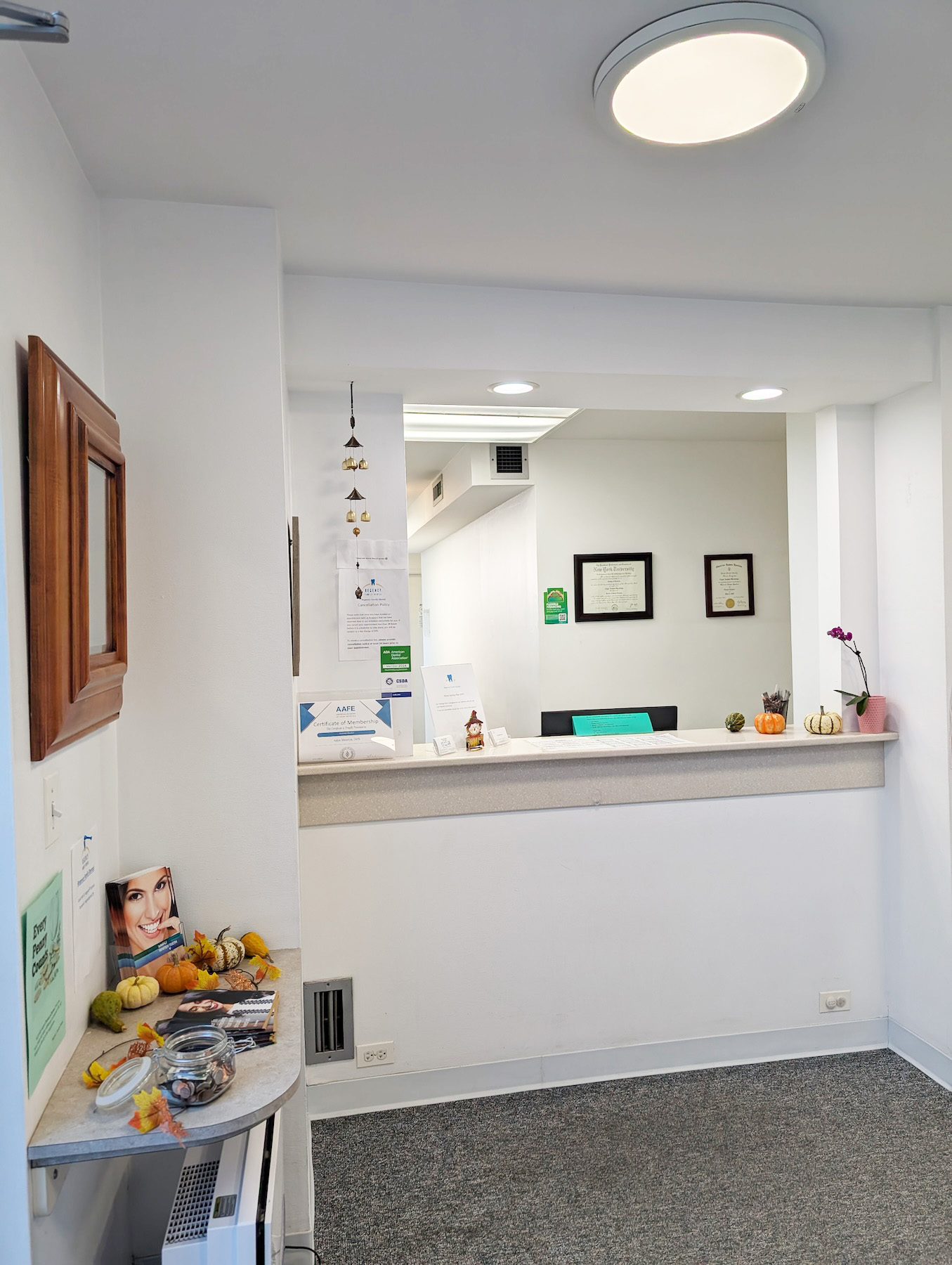 The image shows a well-lit interior space with a reception desk area, featuring a framed picture on the wall above the desk, a round light fixture, and various items on the countertop.