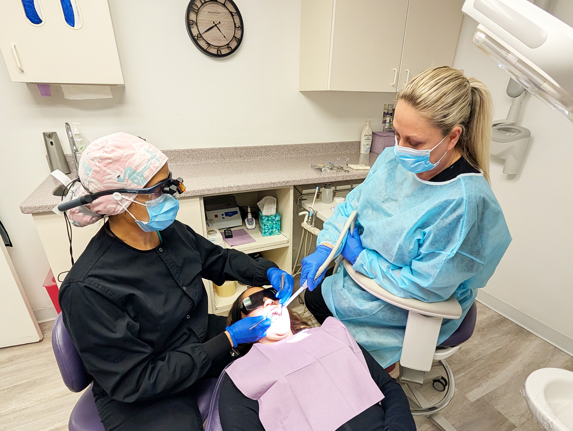A dental hygienist wearing protective gear attends to a patient s teeth in an office setting.