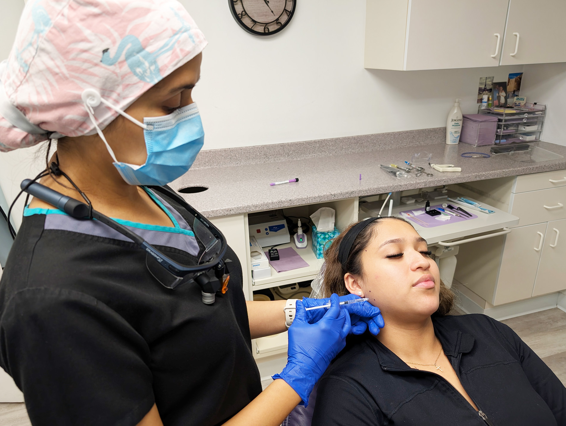 A woman receiving a cosmetic treatment in a dental-like setting with a professional attendant assisting her.