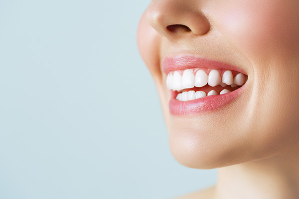 The image features a close-up of a person s smiling face with visible teeth, set against a plain background.