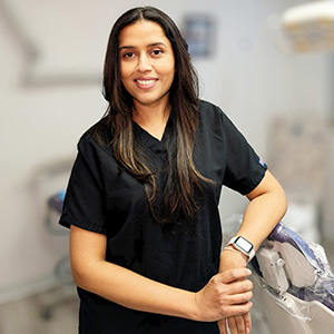 The image shows a woman wearing a white lab coat with a logo on the left chest area, standing against a light background.