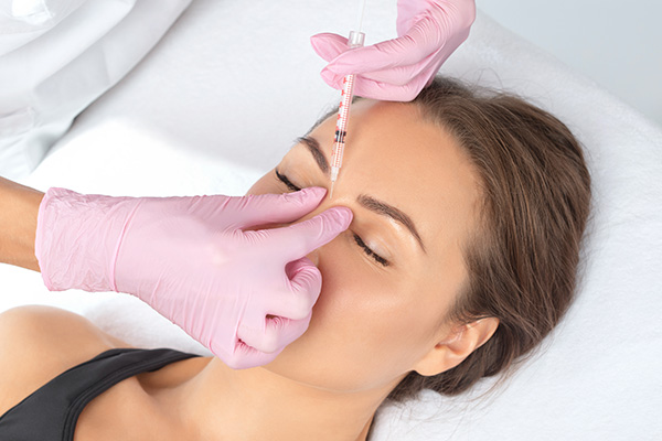 A woman receiving a facial treatment with a needle, under the care of a professional using a magnifying glass.