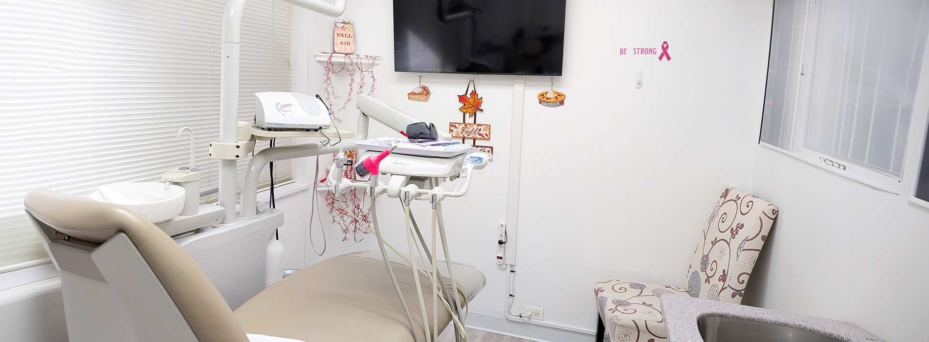 The image shows a well-lit dental office with a clean and modern appearance, featuring a dental chair, a desk with a computer monitor, and various dental equipment visible.