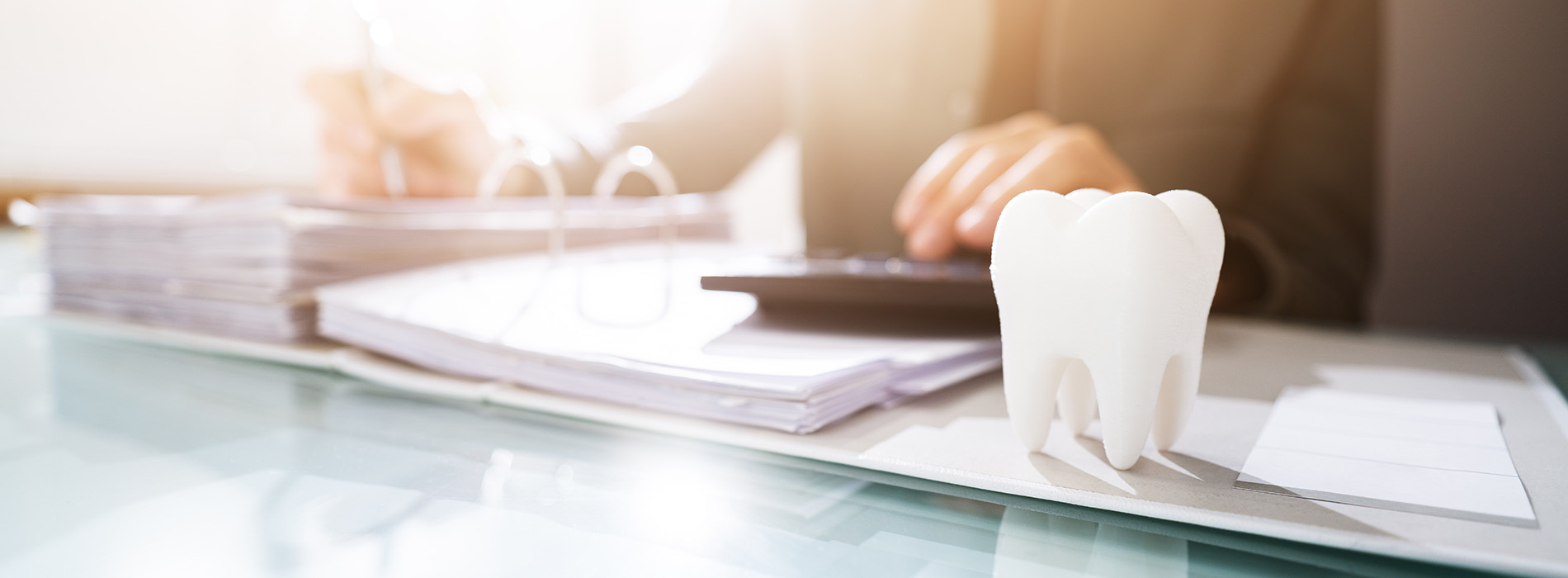 The image shows a close-up view of a person s hands working on a computer, with a blurred background featuring a desk with documents and a model of a human tooth.