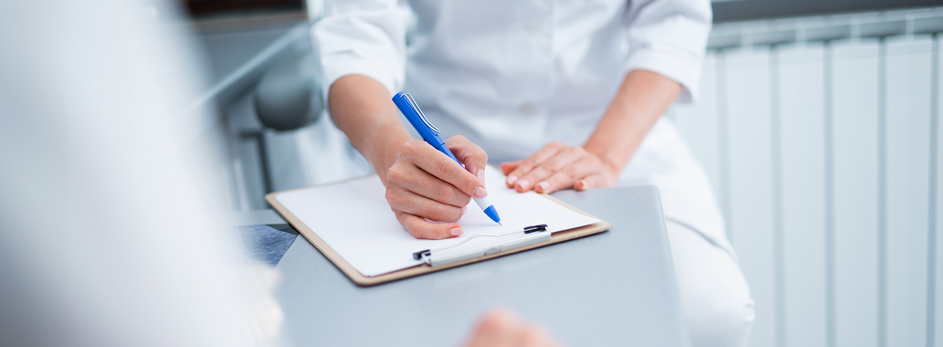 The image depicts a professional setting with a person writing on a clipboard at a desk, surrounded by office furniture and documents, likely engaged in work-related activities.