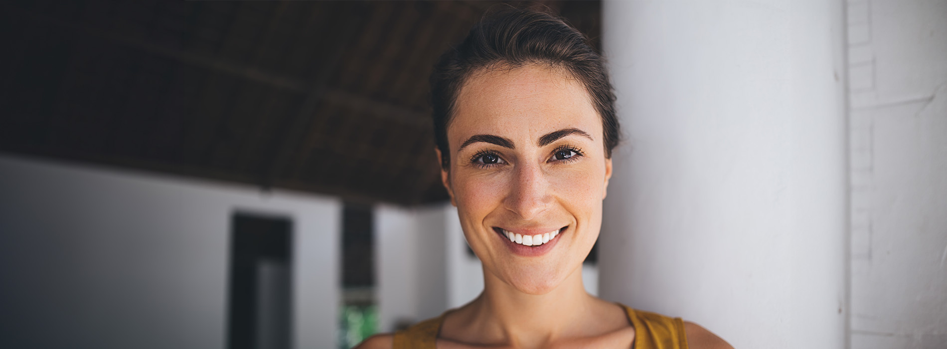 The image shows a woman with short hair smiling at the camera, set against an indoor wall with a wooden texture.