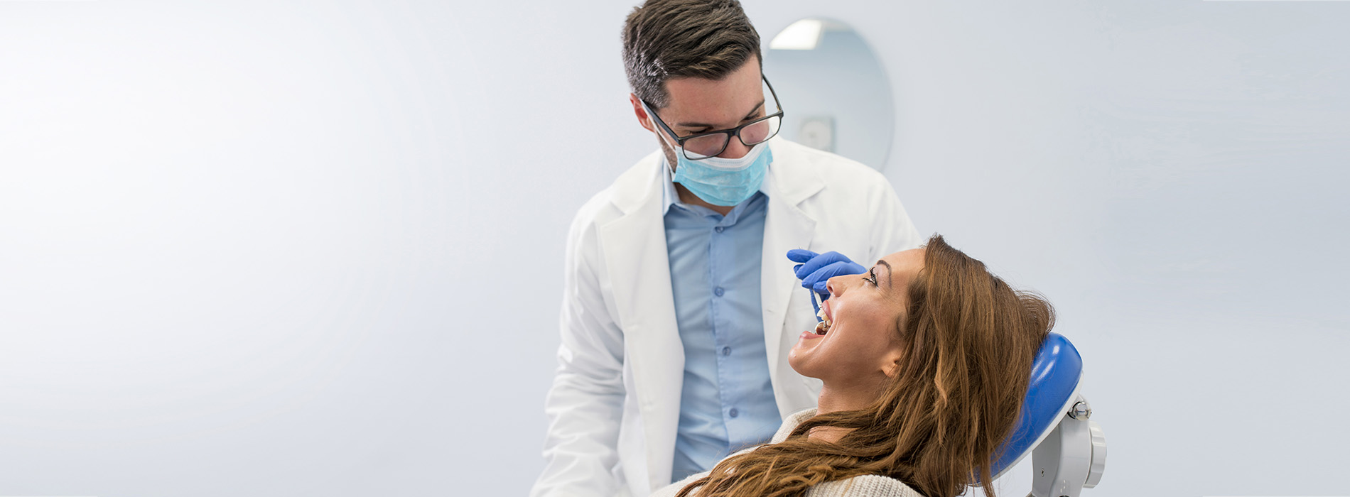 The image shows a dental professional performing oral care on a patient, with both individuals wearing masks and sitting in a dental chair.