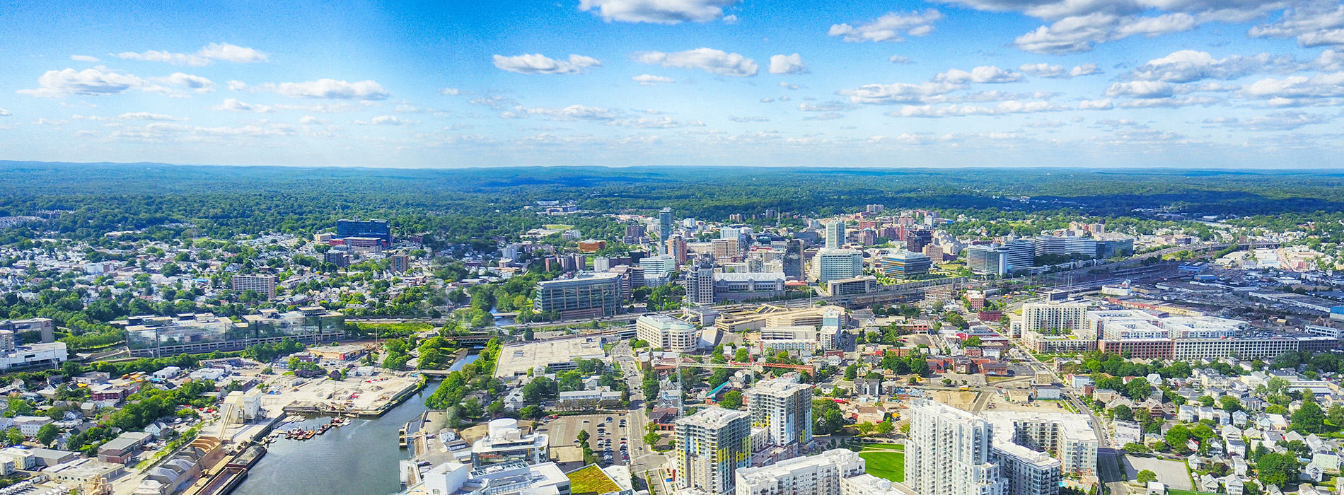 Aerial view of a cityscape with buildings and a river, under a blue sky with clouds.