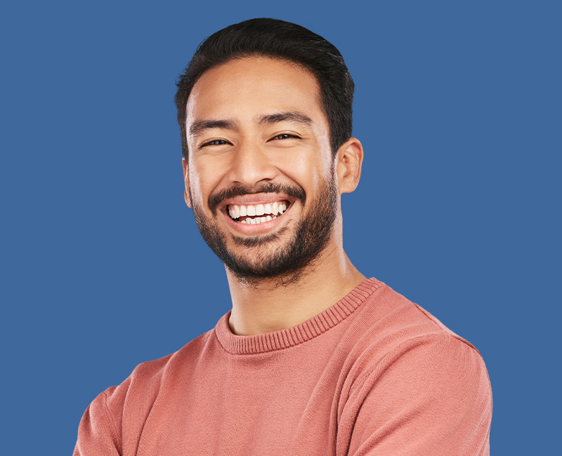 The image features a smiling man with short hair, wearing a pink sweater, standing against a blue background.
