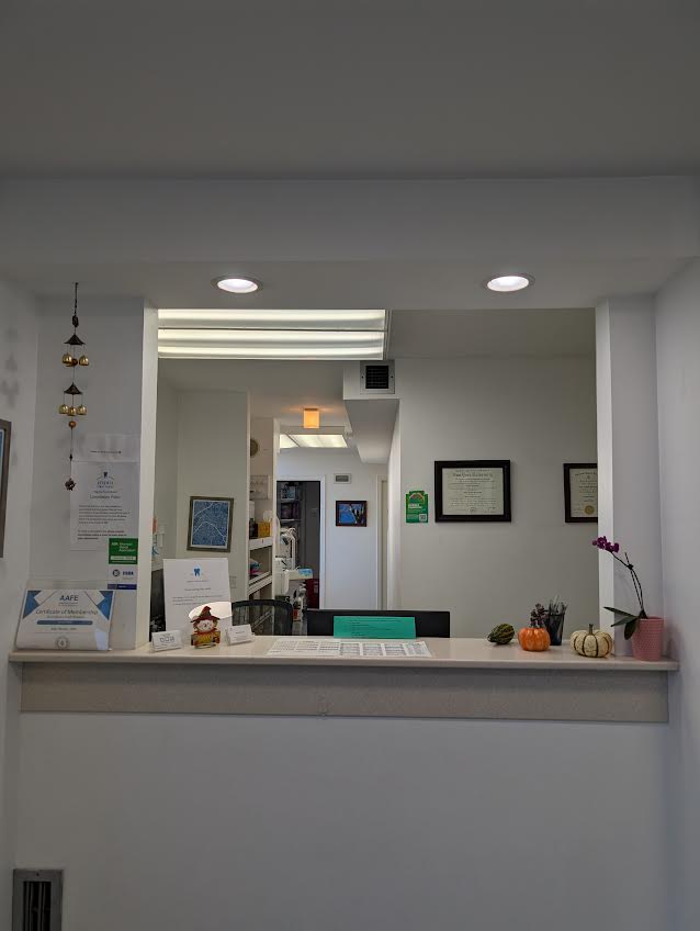 The image depicts an interior view of a room within a building, featuring a reception area with a countertop, signage, and a person seated behind the counter.