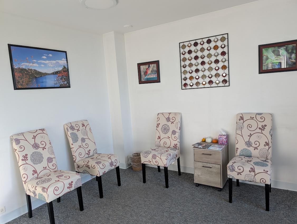 The image shows an interior space with a waiting area featuring a chair, a small table, and decorative elements on the wall, including framed pictures and a board with pins.