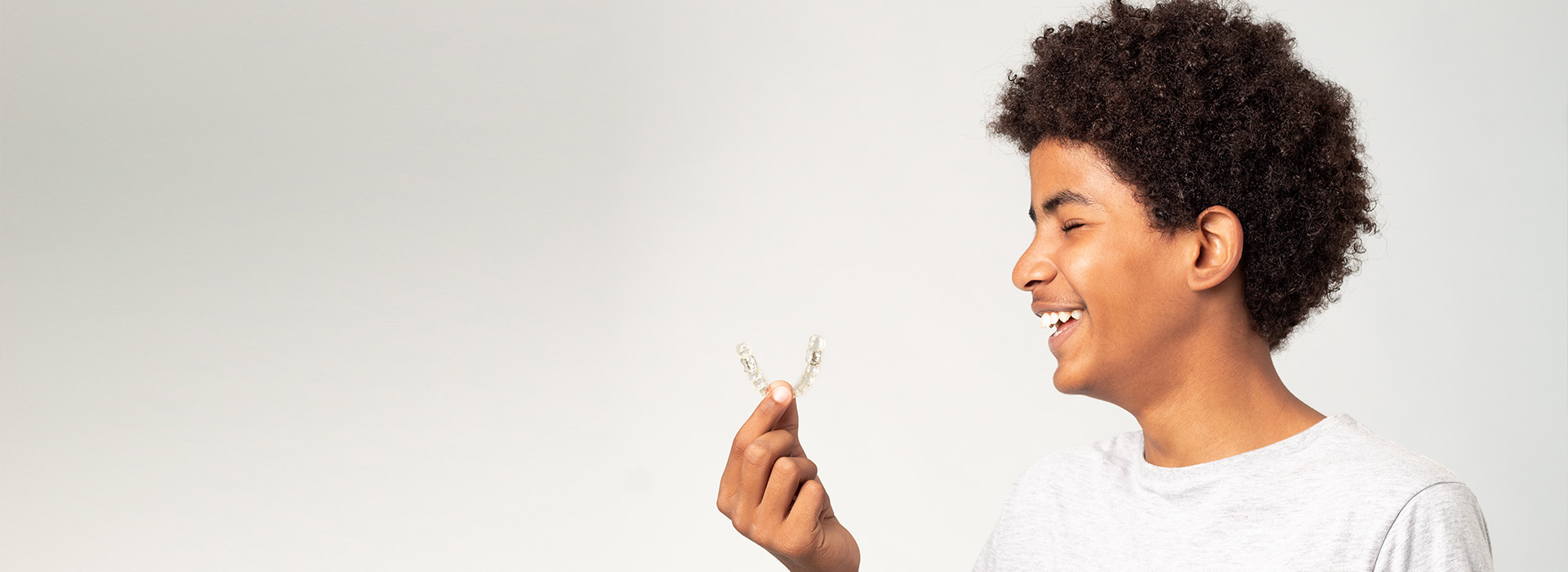 The image shows a young individual holding a flower with a joyful expression, against a plain background.