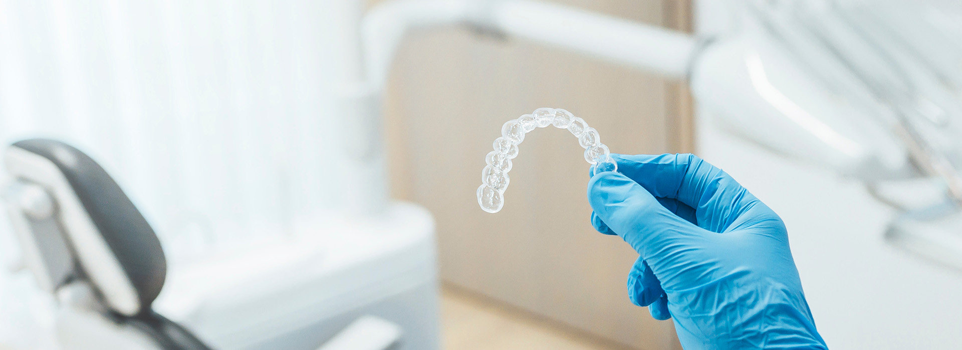 A hand holding a clear plastic object over a dental chair with medical equipment.