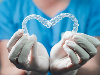 An alternative text description   A person s hands holding a heart-shaped transparent dental retainer against a blue background, symbolizing dental care or love for dental health.