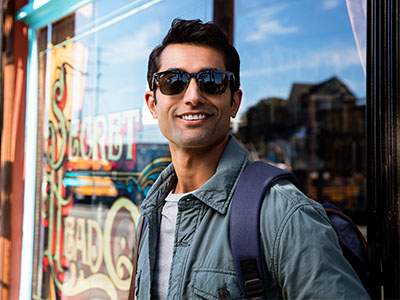 A man wearing sunglasses and a backpack stands outside a shop window with a sign that reads  Sinbad s.