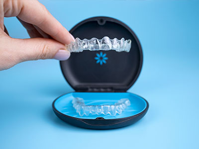 The image shows a person s hand holding an open dental impression tray with a clear resin material inside, revealing a blue base for the teeth, next to a black case that appears to be the lid of the same dental impression kit.