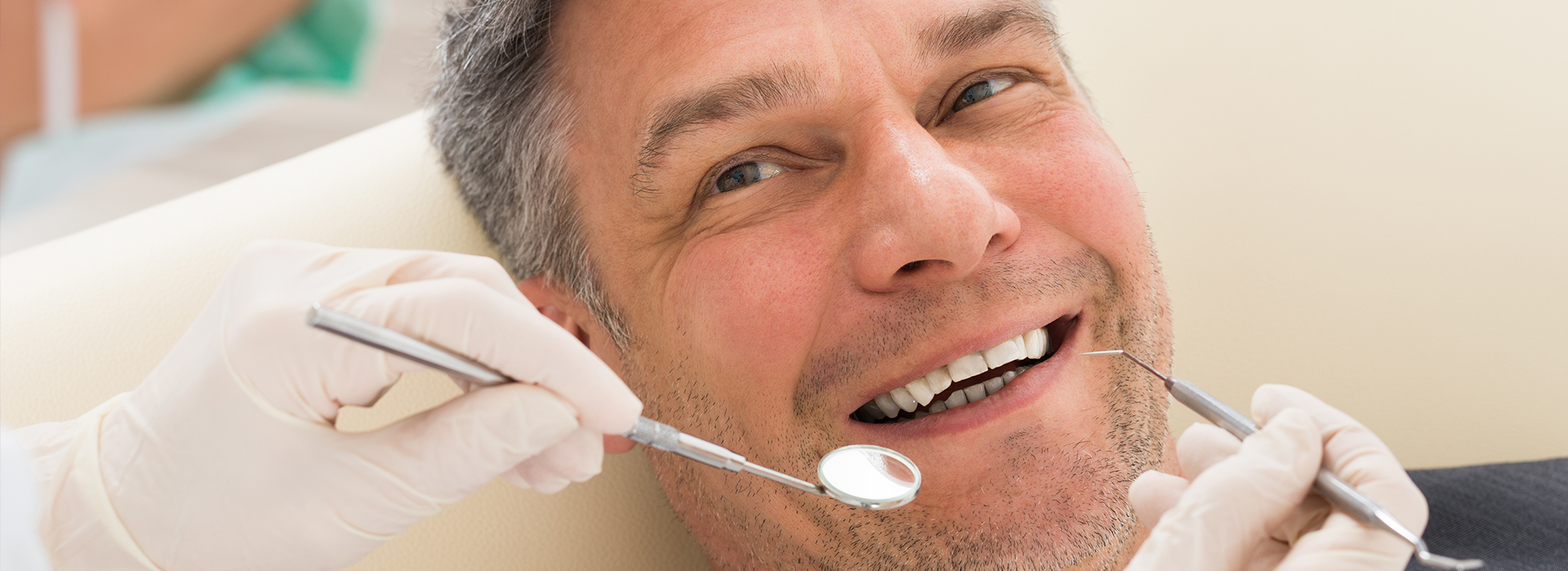 A man receiving dental treatment with a smiling expression while seated in a dental chair, surrounded by dental instruments and equipment.