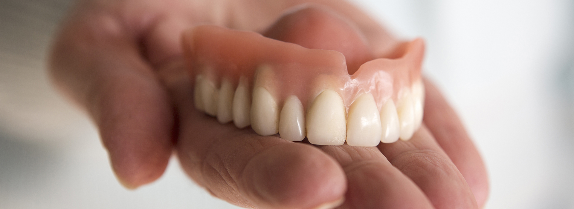 The image shows a person holding a set of dentures with an artificial mouth structure, emphasizing the dental appliance s shape and features.