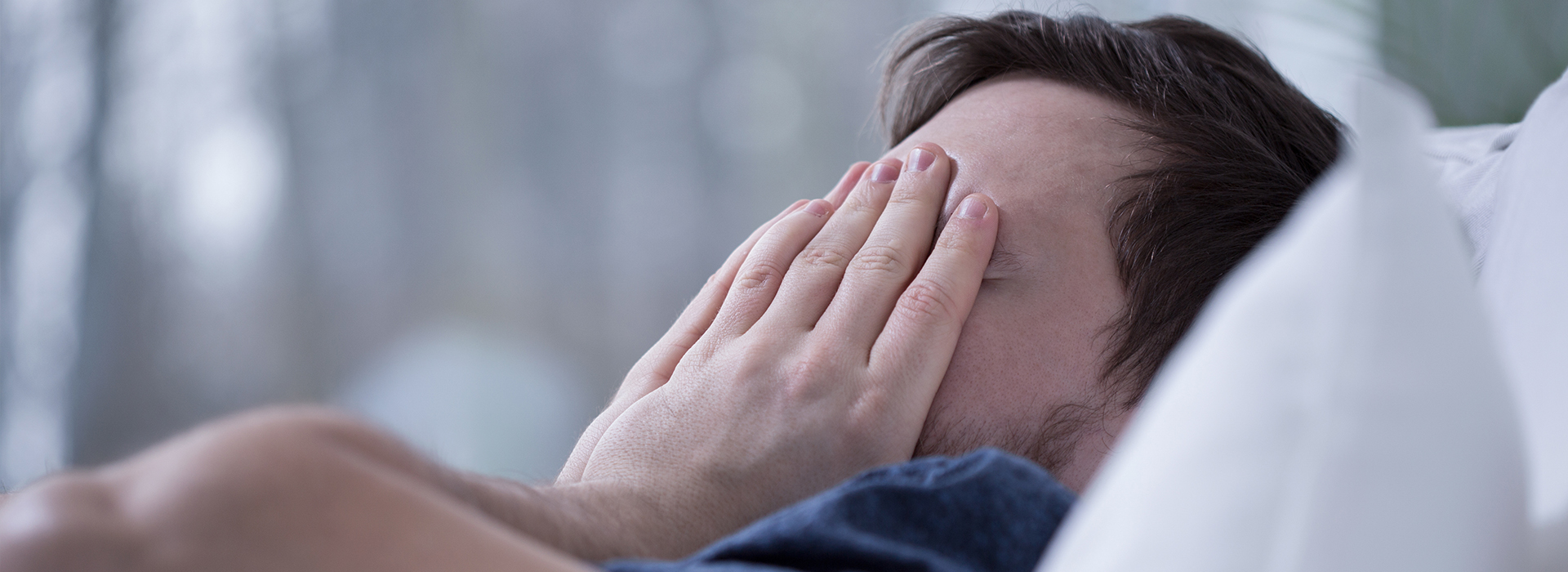 The image shows a person lying on their side with their head resting on their hand, appearing to be in a state of distress, possibly crying or upset, with a blurred background that suggests an indoor setting.