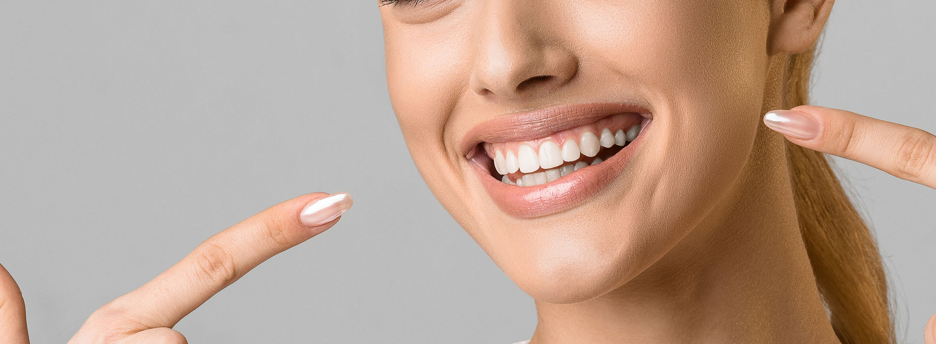 The image shows a woman with a radiant smile, holding her fingers up to her cheeks, against a neutral background.