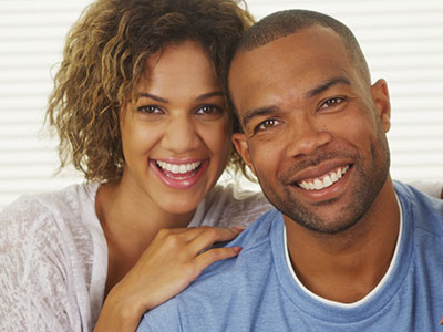 A man and woman smiling at the camera, sharing a happy moment together.