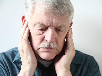 The image shows an older man with his eyes closed, holding his hand to his ear, appearing to be asleep or resting, with a look of concern on his face.